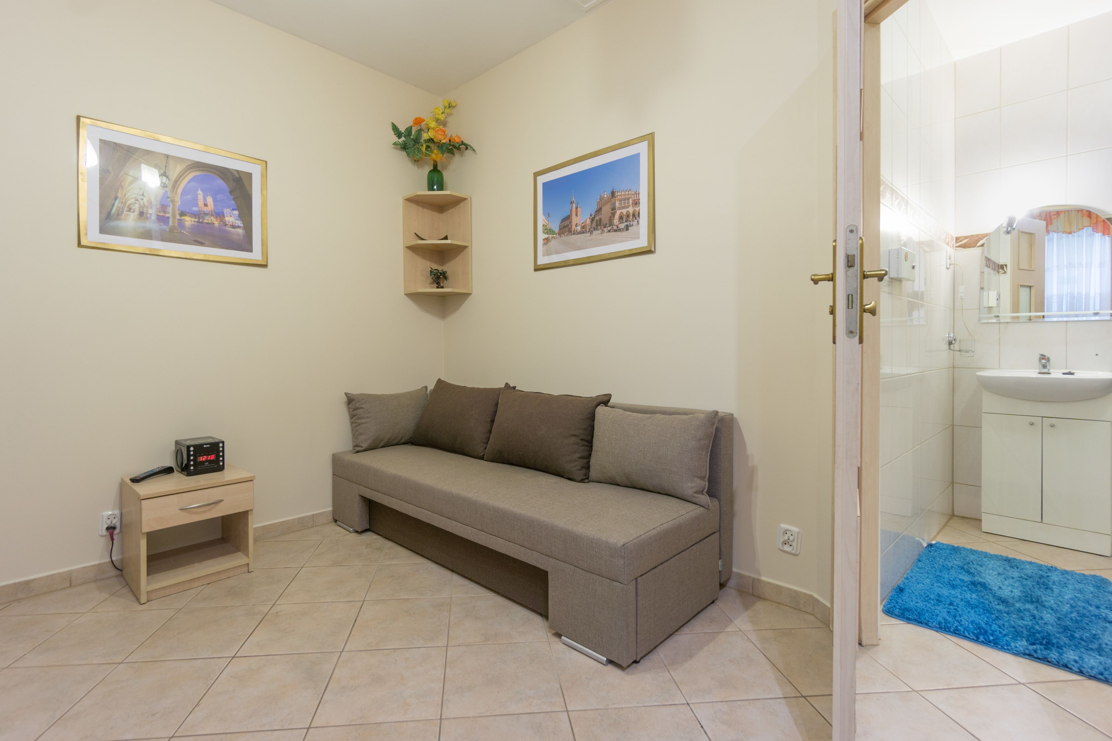 Een woonkamer met een bank, een klein tafeltje met een radio, en twee ingelijste foto's aan de muur.