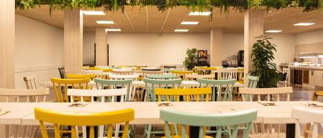 A cafeteria with multiple tables and chairs, some with yellow and white chairs, and a ceiling decorated with greenery.