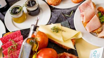 Diverse etenswaren op een tafel, waaronder brood, kaas, tomaten en gerookt vlees.