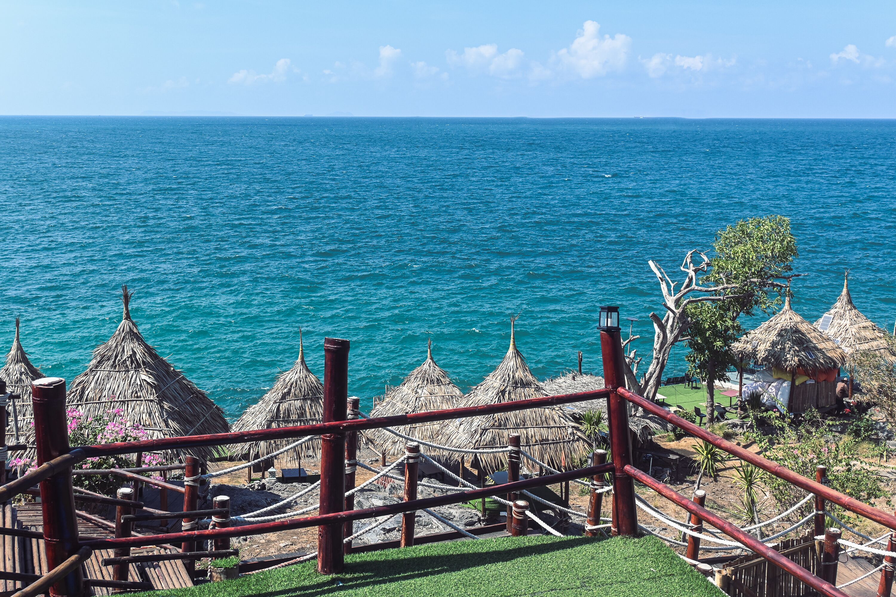 A view of a beach with thatched huts and a wooden deck overlooking the ocean.