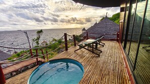 Terraza de madera con piscina, sillas de descanso y una estructura de techo de paja con vistas al mar.