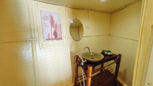 Un baño con un taburete de madera, un lavabo con un recipiente verde y un espejo en la pared.