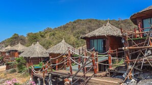Varias cabañas con techo de paja, barandillas de madera y una terraza, rodeadas de paisaje natural.