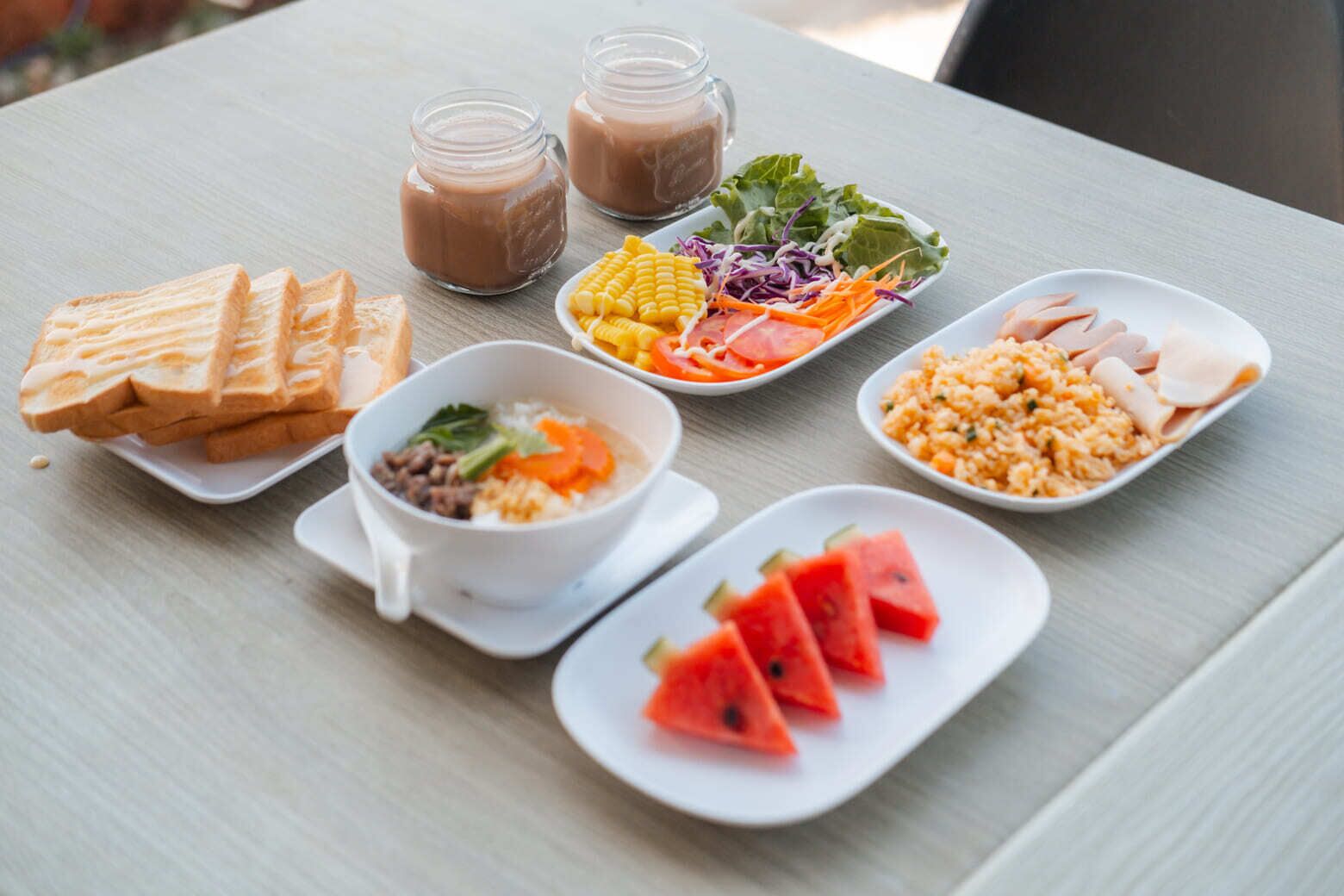 Ein Tisch mit verschiedenen Speisen, darunter Toast, Suppe, Salat, Reis und Wassermelonenscheiben.