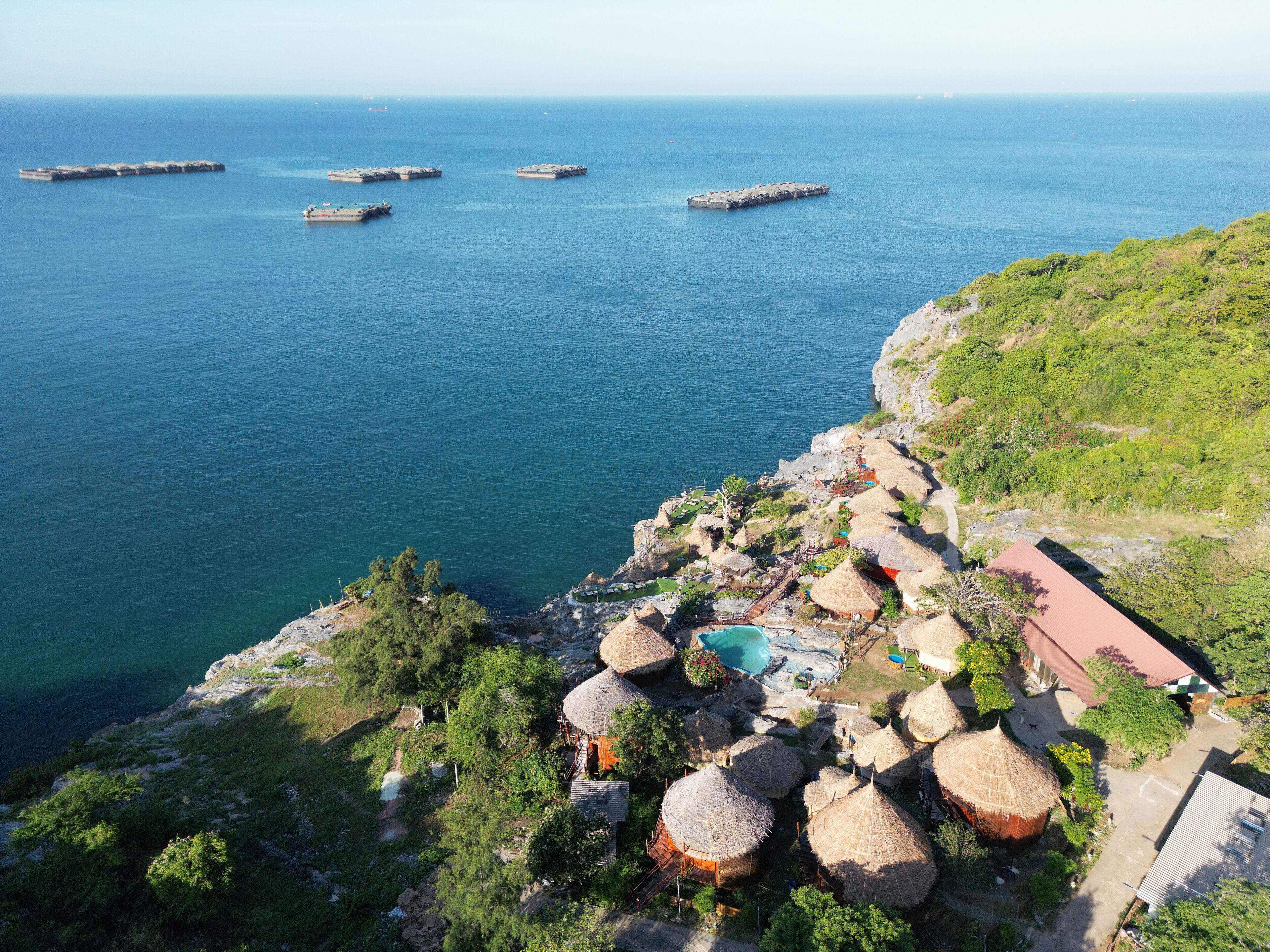 A coastal resort with thatched-roof huts, a swimming pool, and a view of the sea.