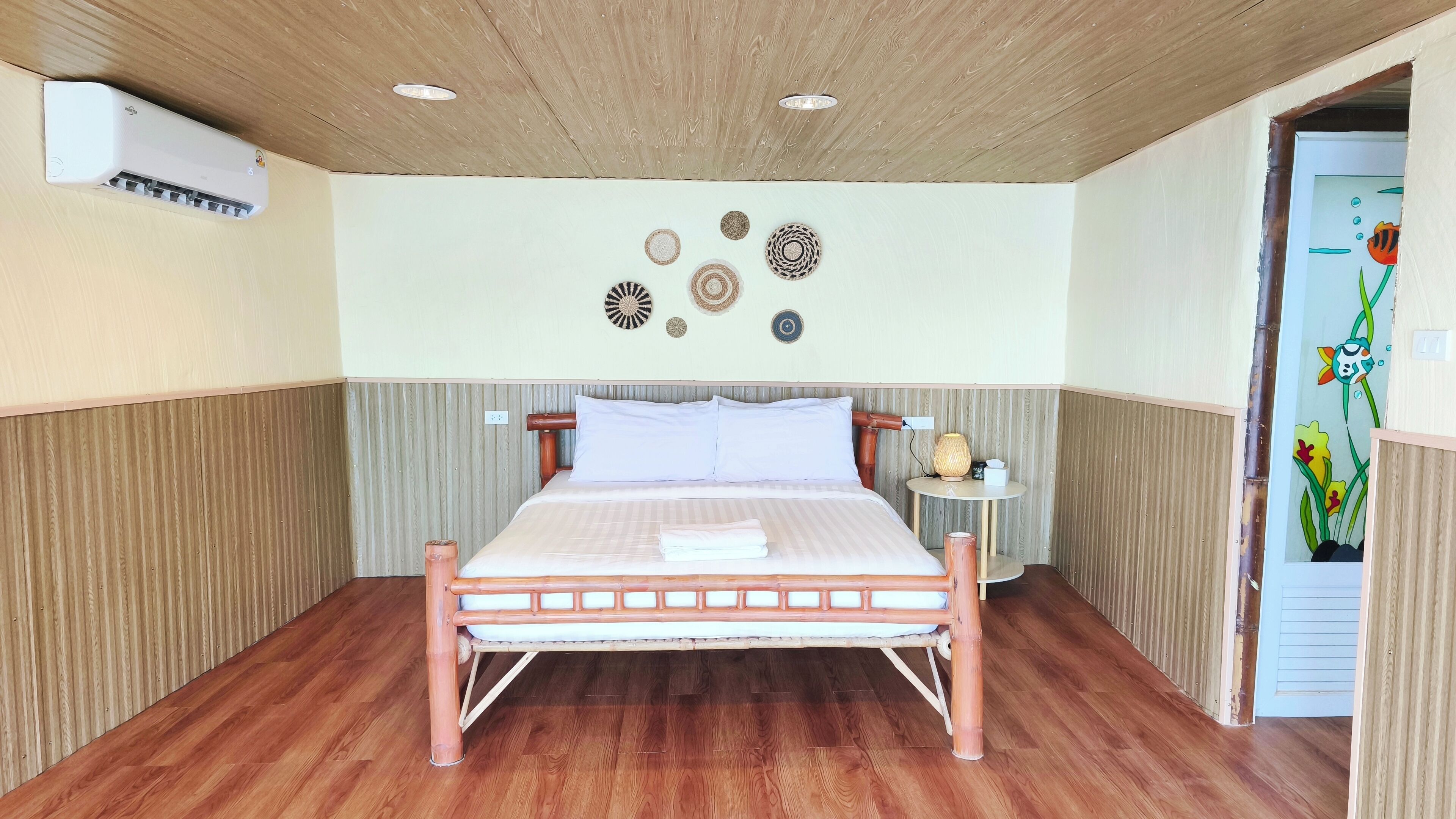 Quarto com cama de madeira, mesa de cabeceira com abajur e decoração nas paredes.