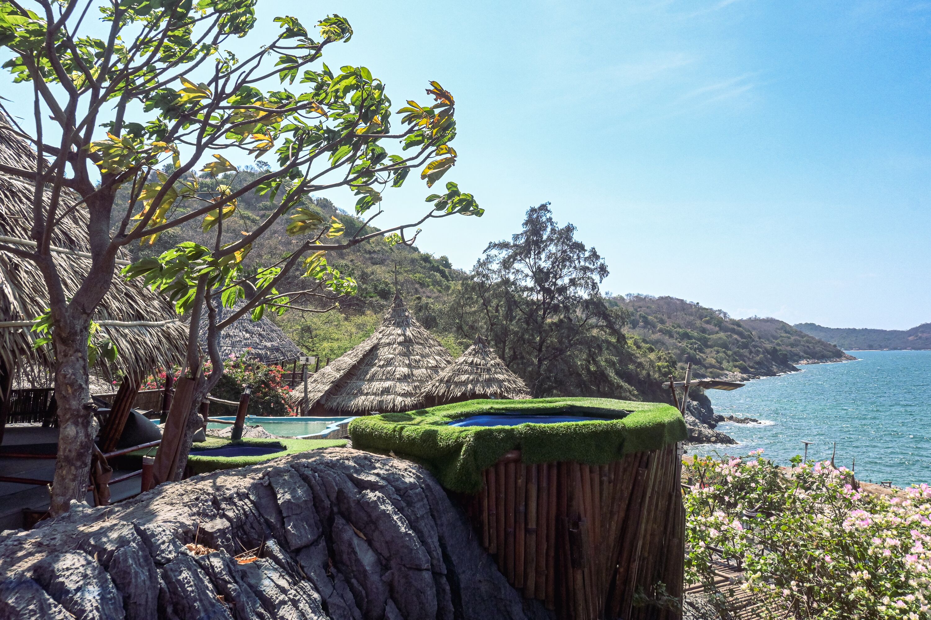 Ein Küstenresort mit einem strohgedeckten Gebäude, einem Swimmingpool und Blick auf das Meer.