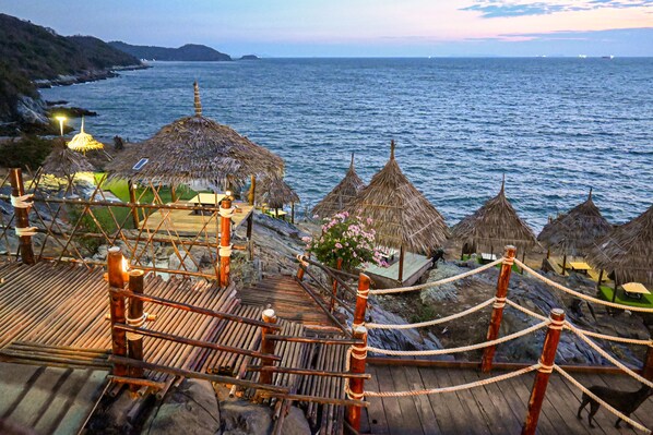 A wooden deck with rope barriers leading to thatched-roof huts overlooking the sea.