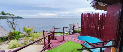 Zona de piscina con vista al mar, terraza de madera y construcción con techo de paja.