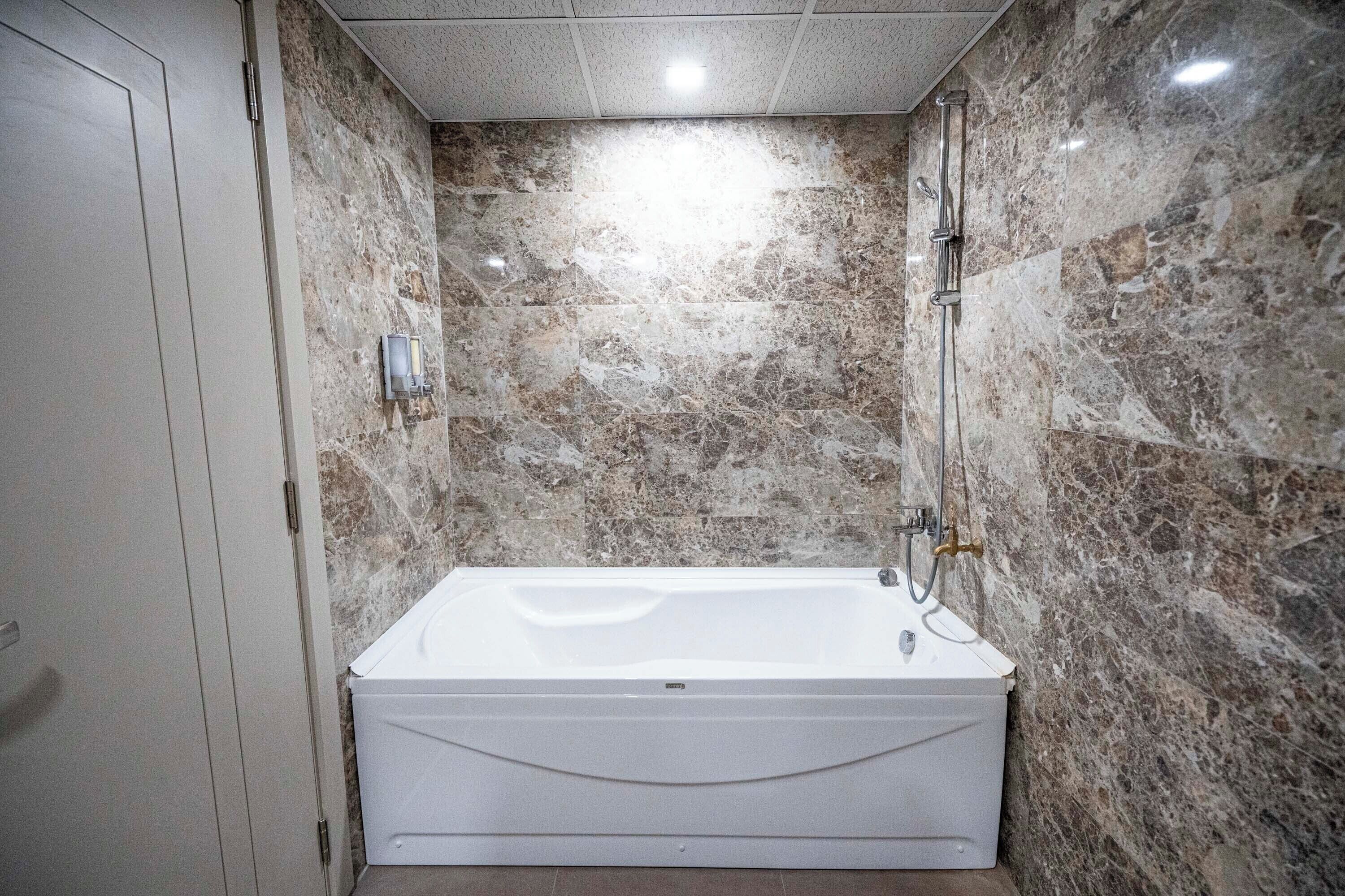 A bathroom with a marble wall, a white bathtub, and a shower area.