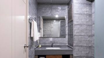 A modern bathroom with a grey tiled floor, a white toilet, a grey sink with a mirror above it, and a towel rack with white towels.