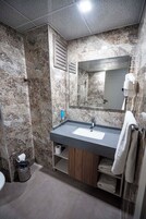 Un baño con pared de mármol, un lavabo con espejo, un perchero y un cesto de basura.