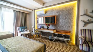 A hotel room with a bed, a desk, a chair, a TV, and a small table with a vase of flowers.