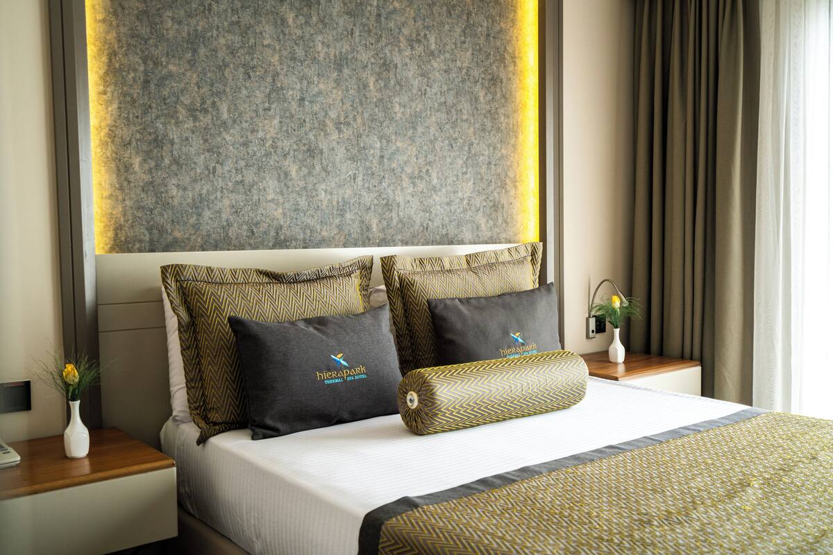 Habitación de hotel con una cama grande, dos mesitas de noche, un florero con flores y una lámpara fijada a la pared.