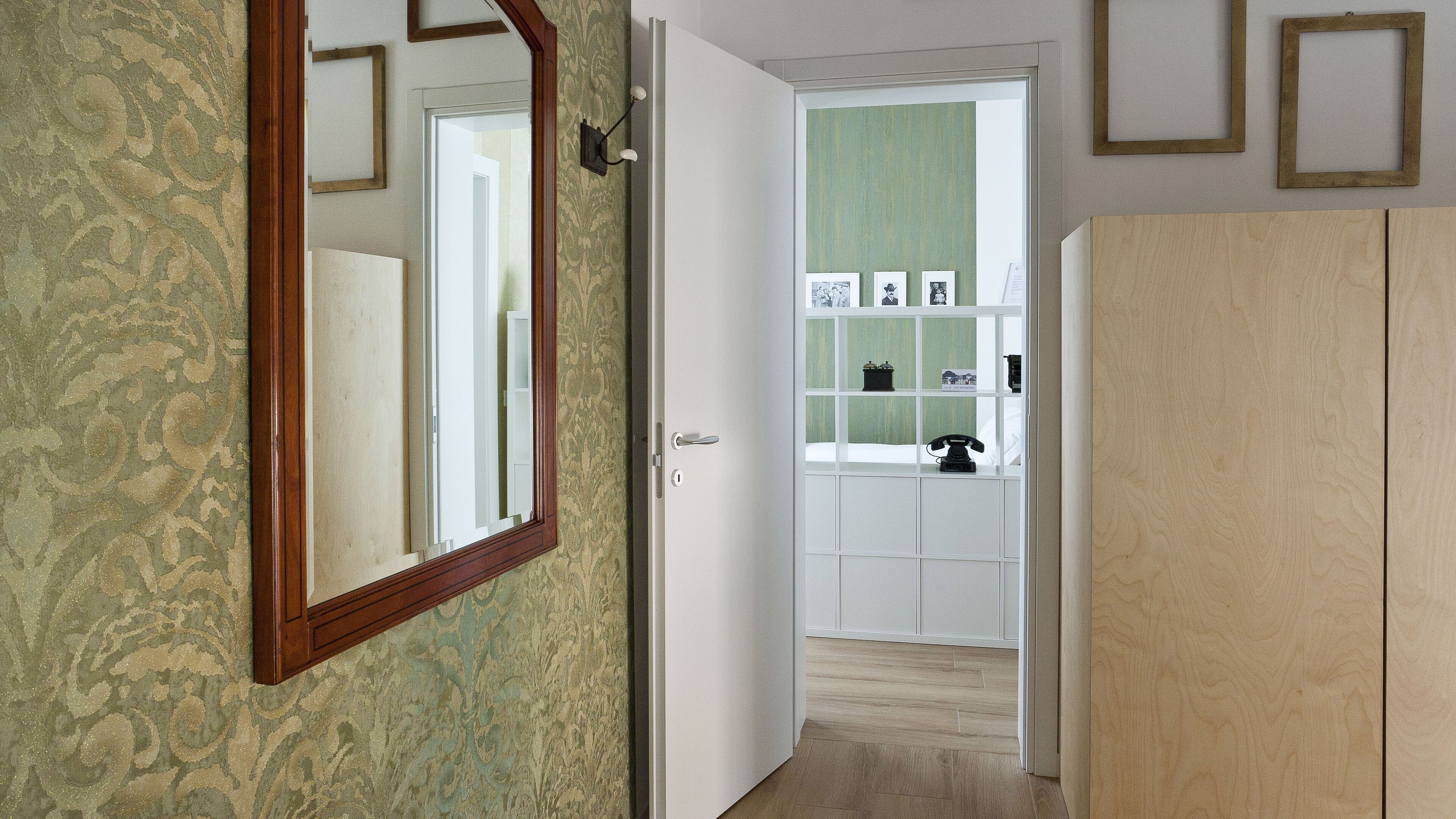 A hallway with patterned wallpaper, a wooden door, and a white cabinet.