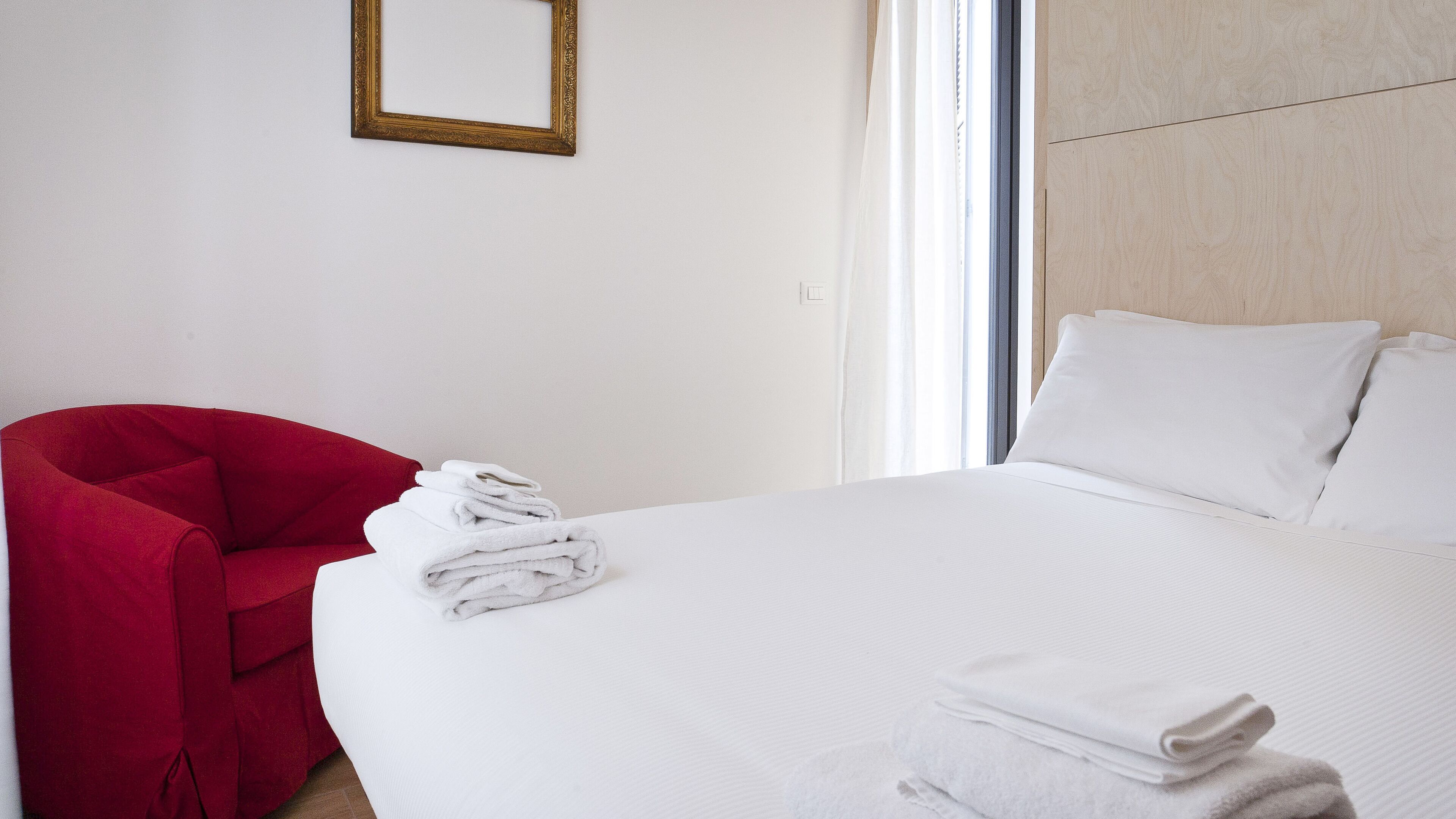 Une chambre d’hôtel avec un lit, une chaise rouge et une pile de serviettes blanches.