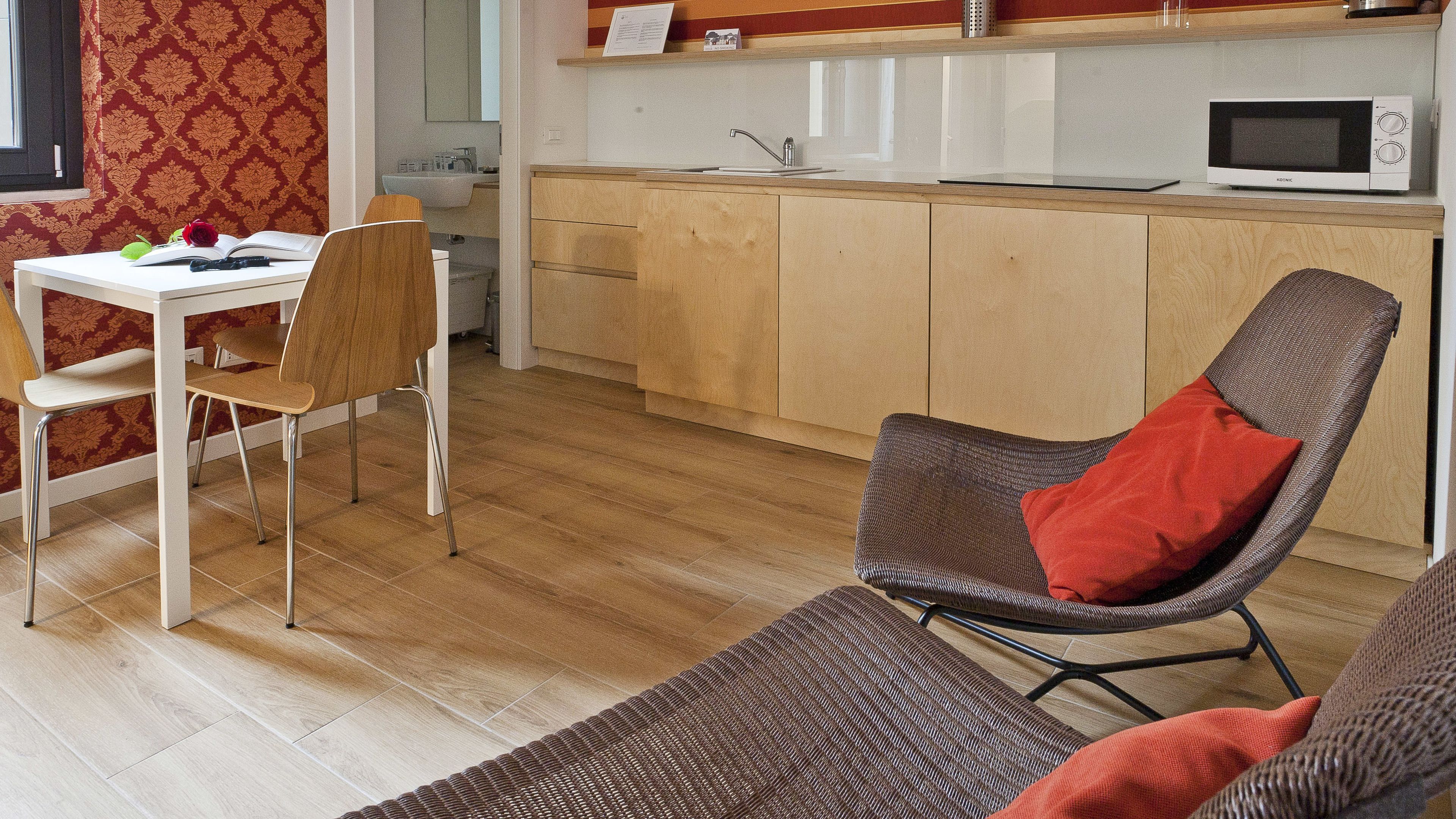 A compact living space with a dining area, a kitchenette, and a seating area with a brown chair and a red pillow.
