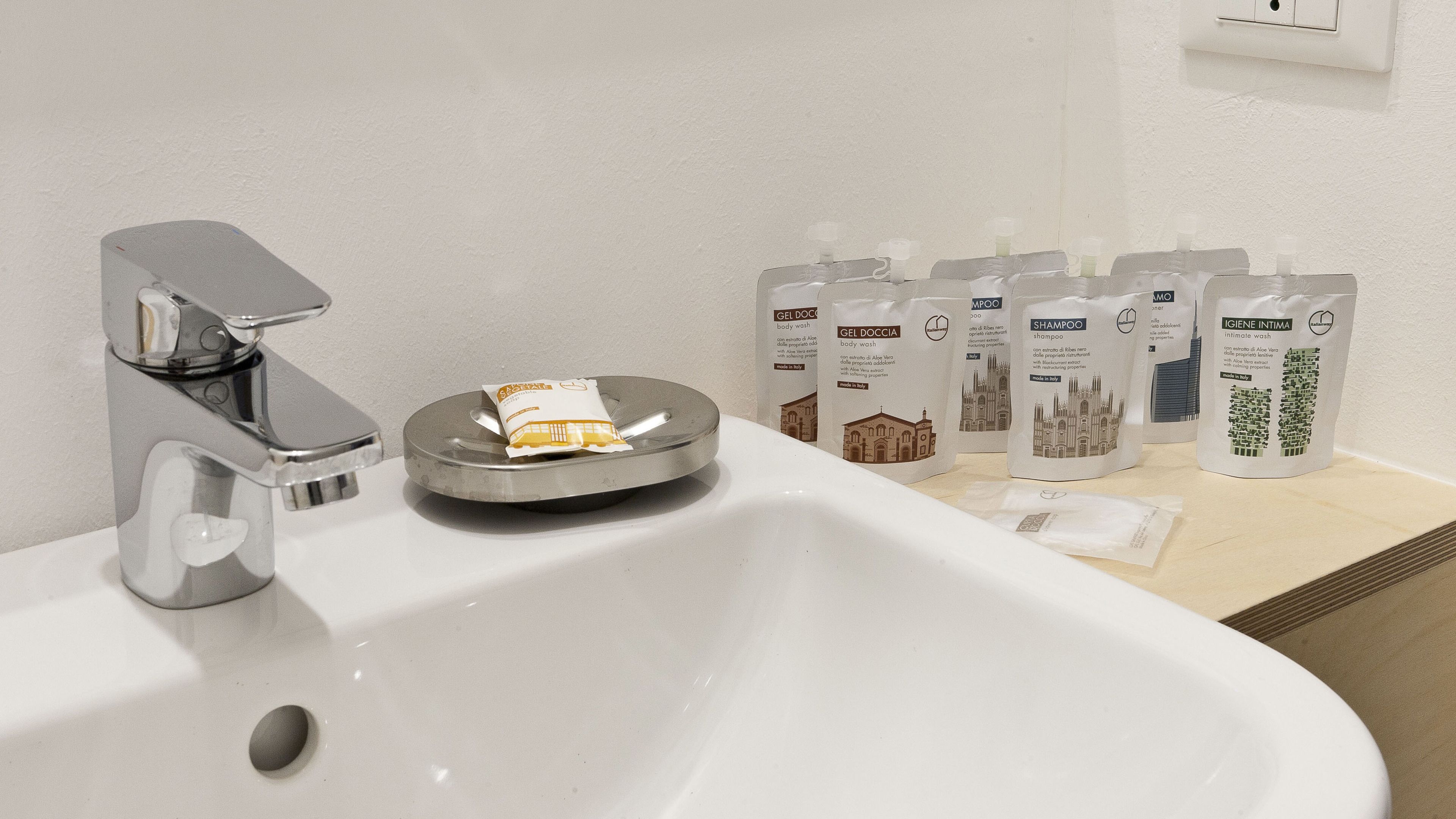 A bathroom sink with a chrome faucet, a soap dish, and several bottles of toiletries including body wash, shampoo, and intimate wash.