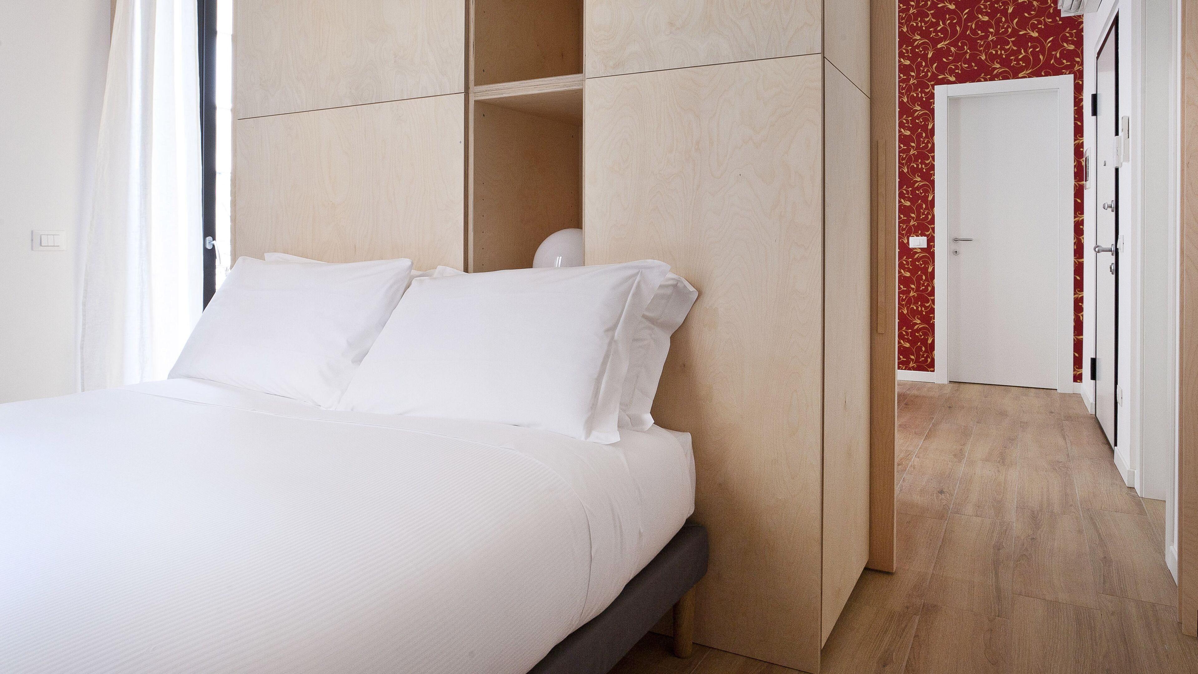 Un dormitorio con cama, armario y puerta, con pared decorada con un estampado rojo.