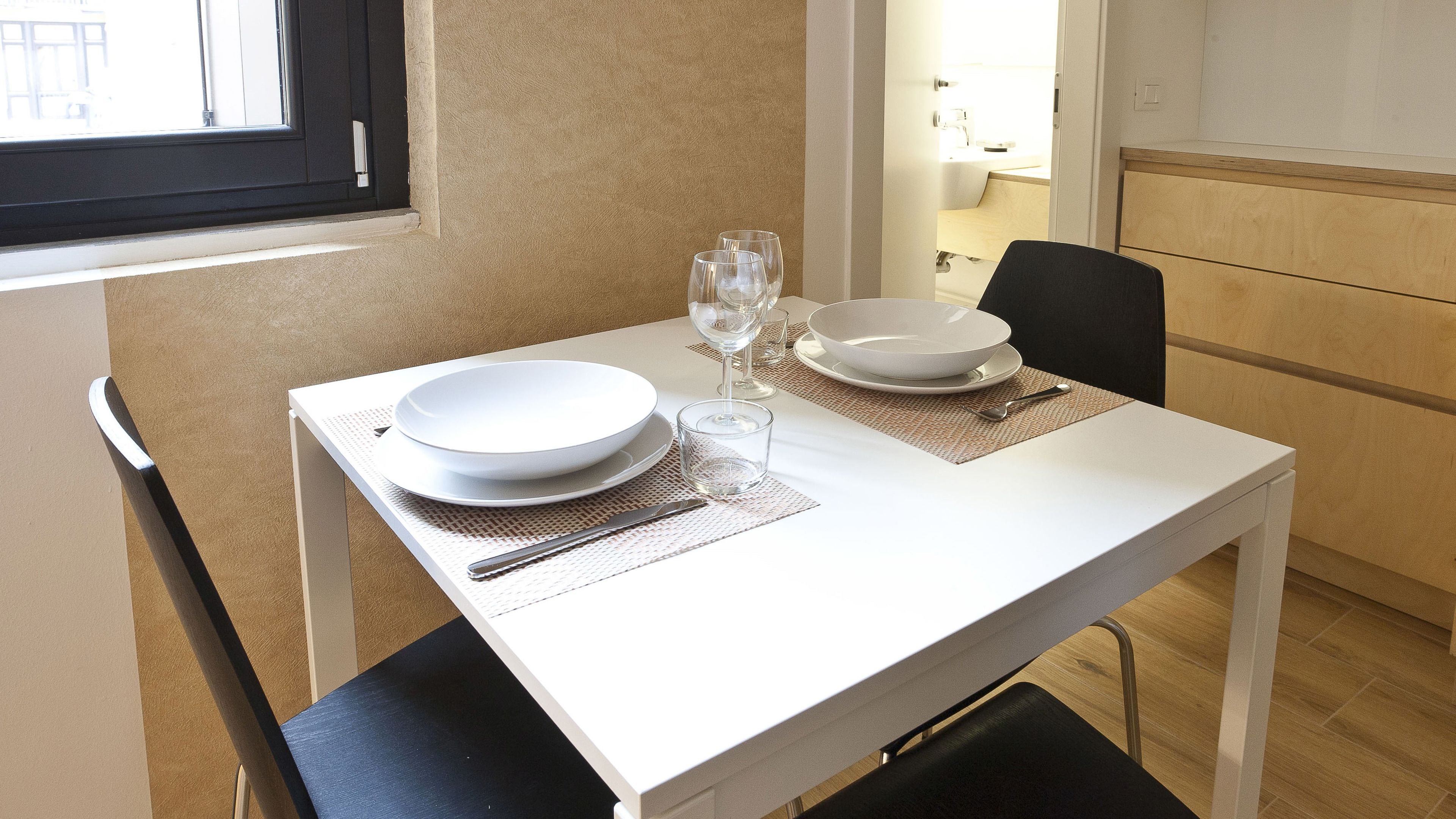 A dining table set with white plates, bowls, and cutlery, with a window and a view of the outside.
