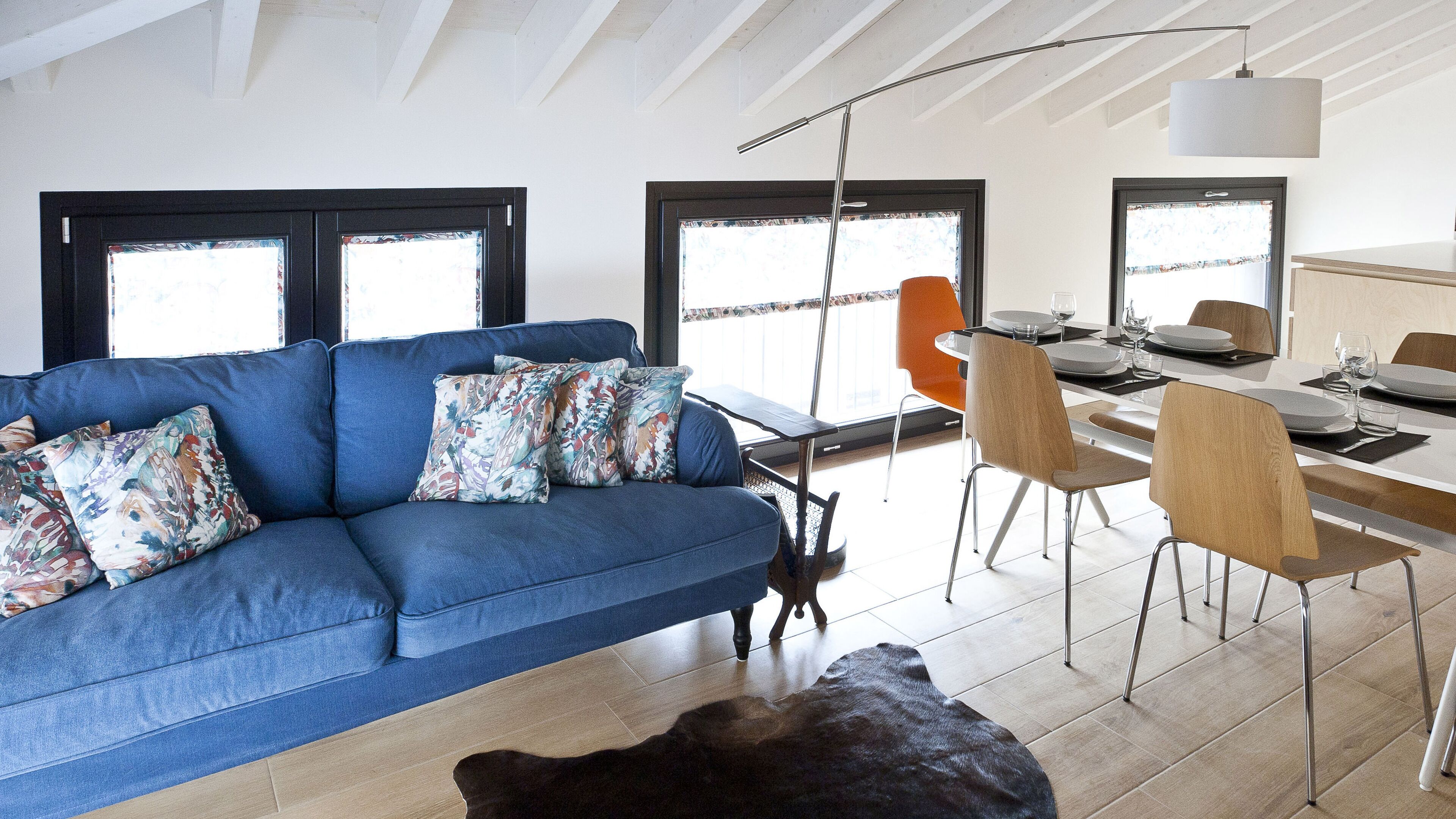 A modern living room with a blue sofa, a dining table set for four, and a large window with a view.