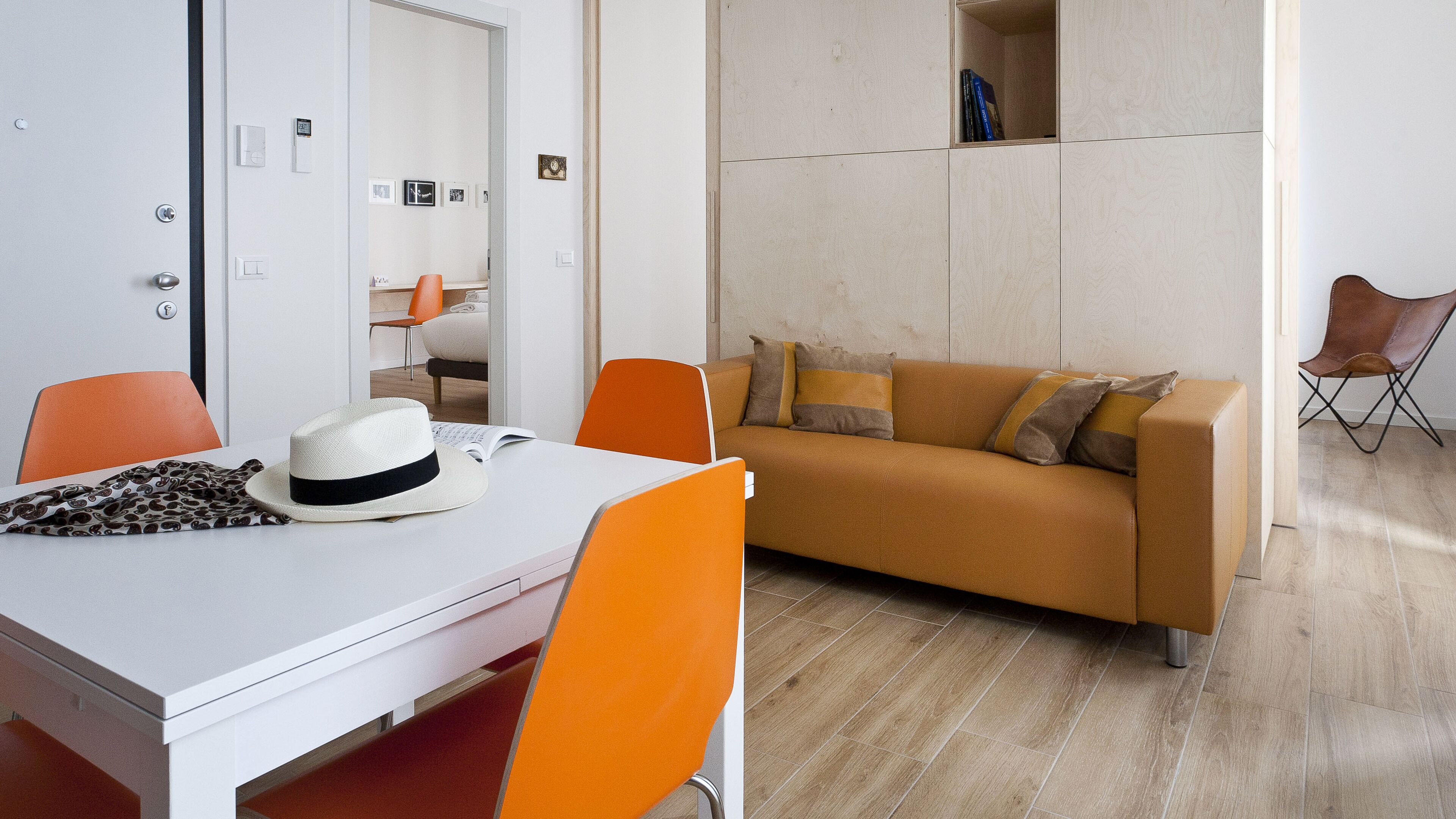 A modern room with a white table, orange chairs, a brown sofa, and a wooden floor.