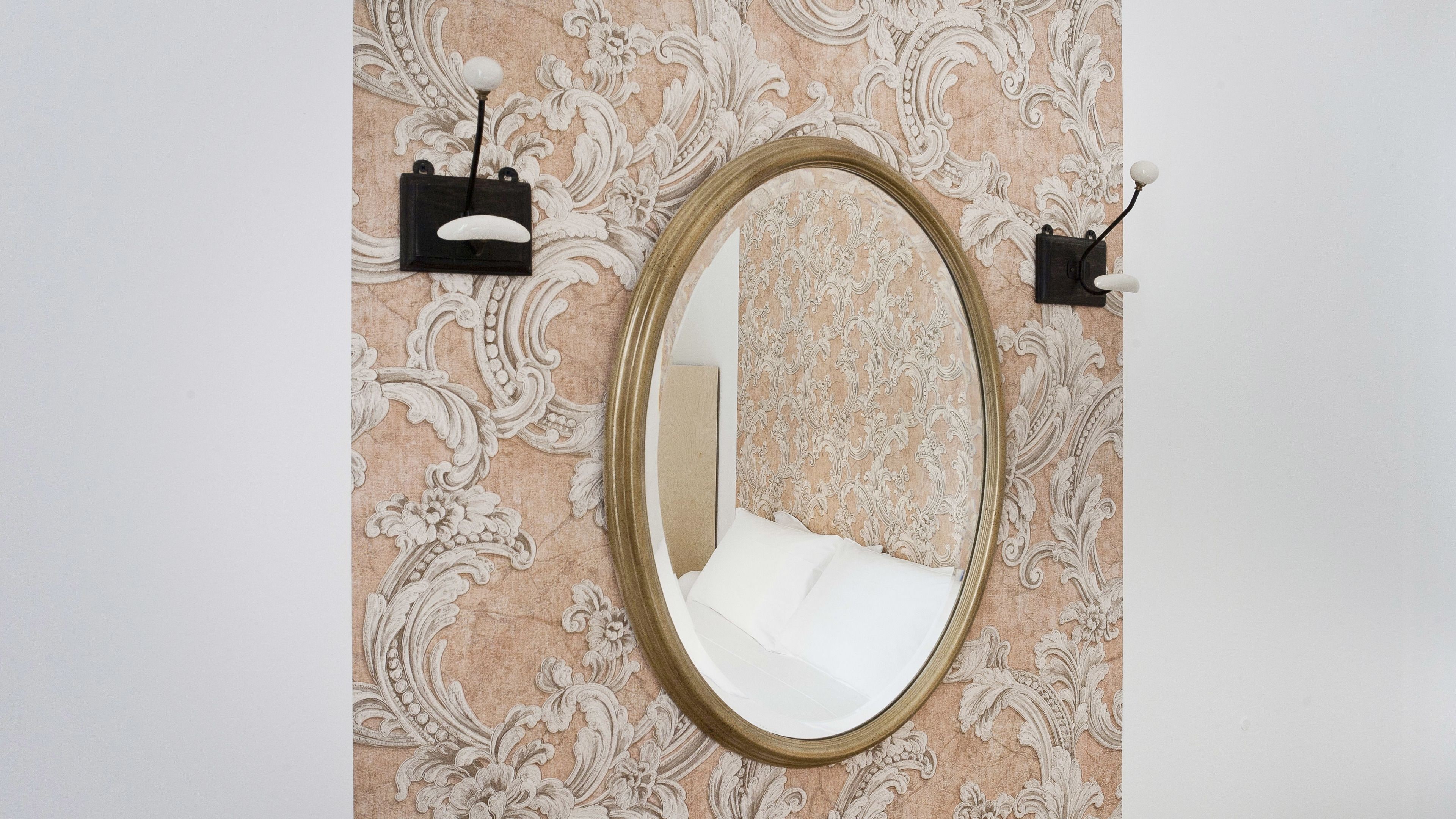 A mirror with a gold frame on a wall with ornate wallpaper.