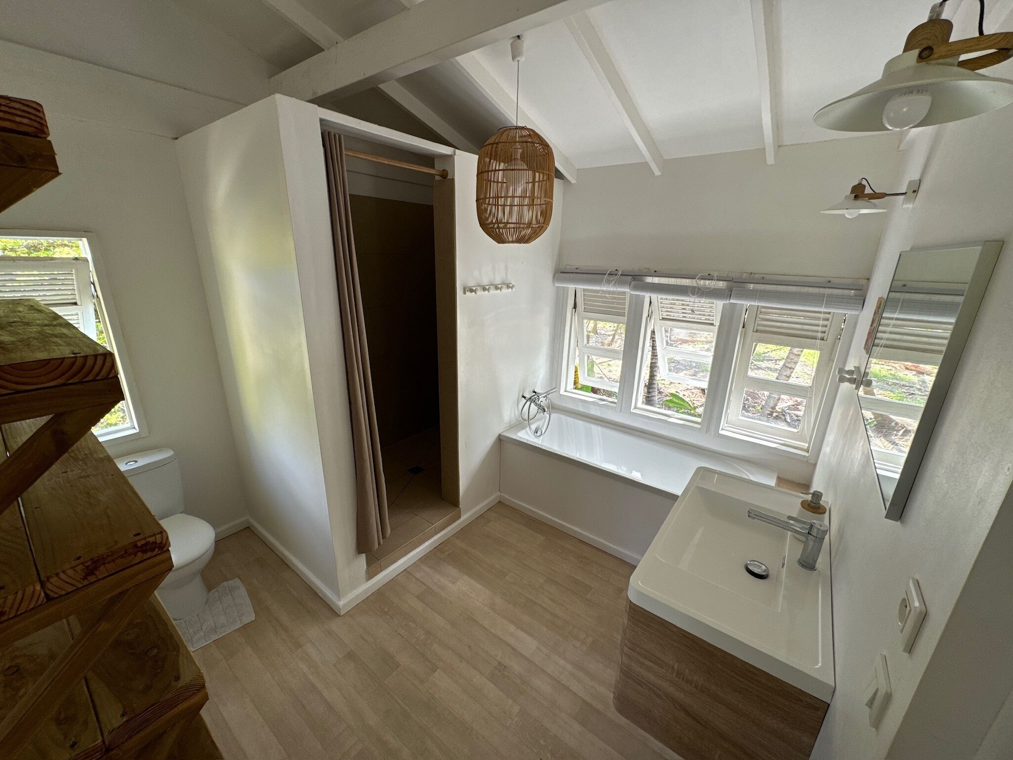 A modern bathroom with a wooden floor, a white sink, a large window, and a shower area.