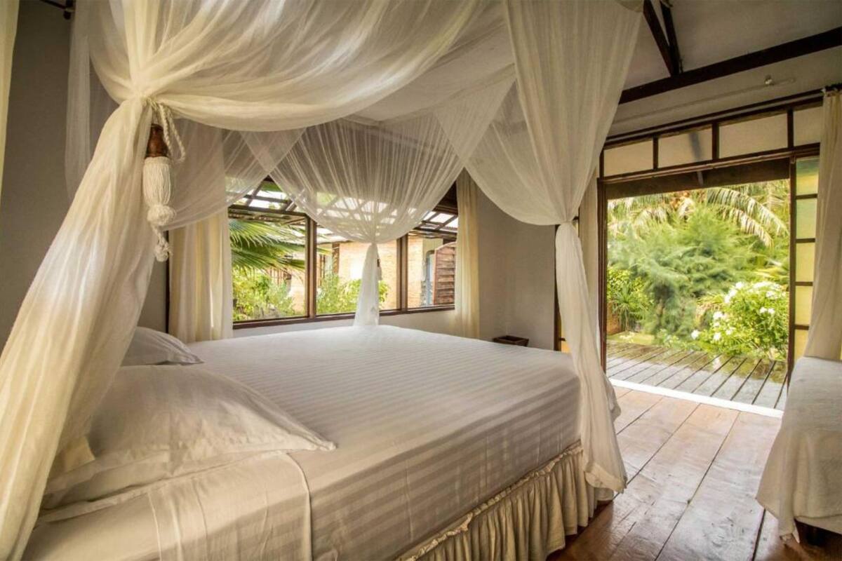 Quarto com cama grande, roupa de cama branca e dossel.