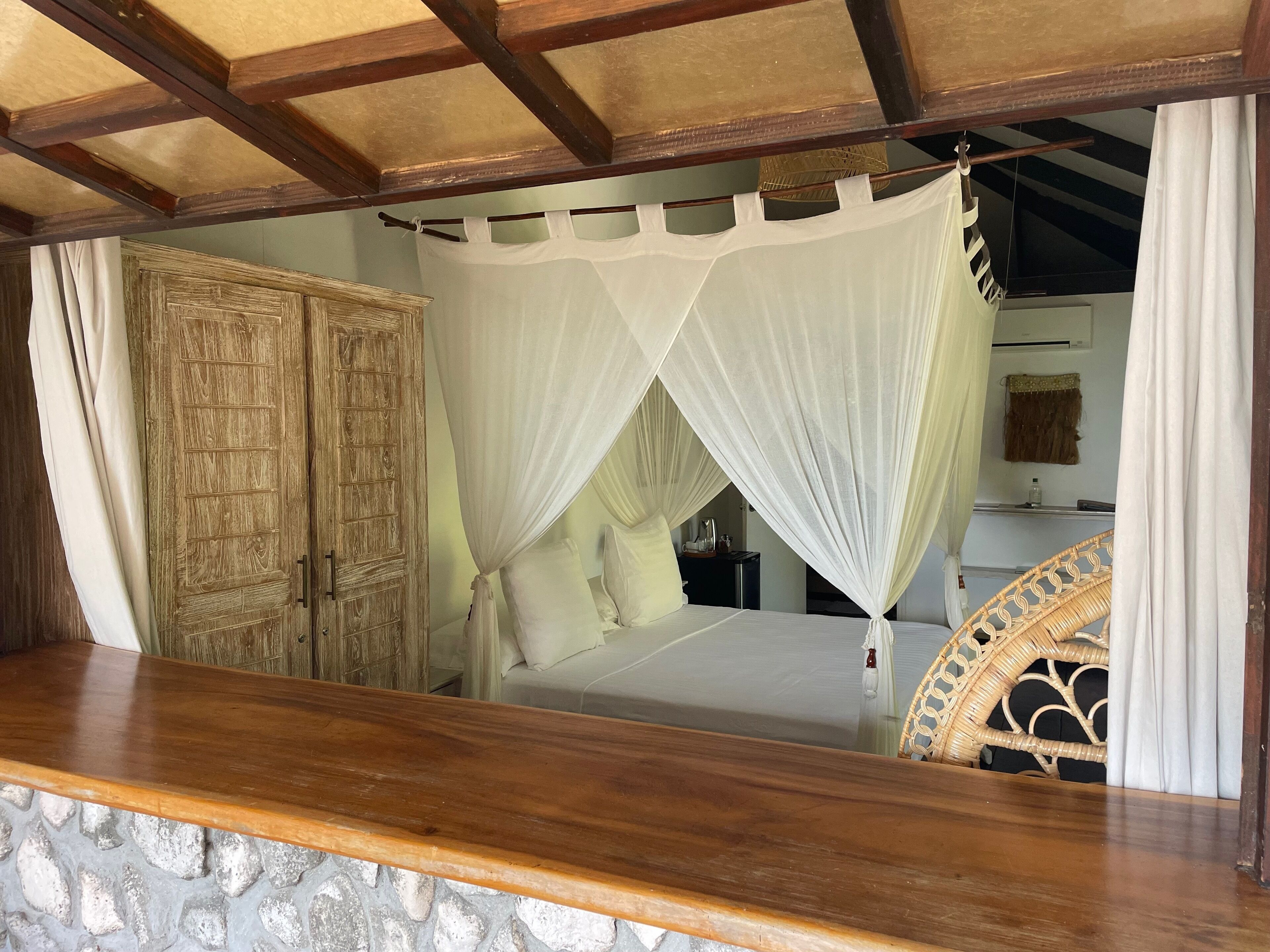 A bed with a canopy, a wooden wardrobe, and a stone wall.