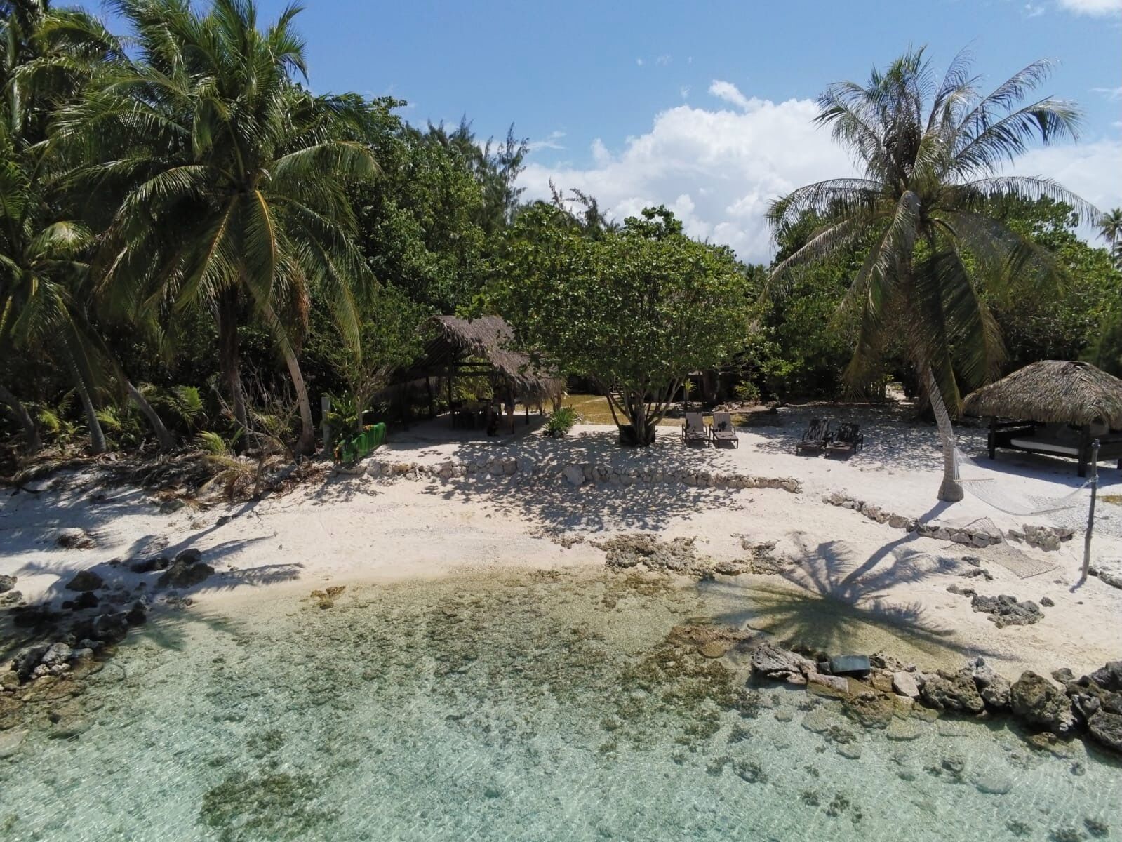 A beach with clear turquoise water, palm trees, and thatched-roof structures.