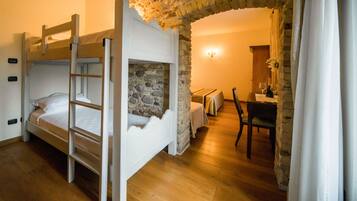 A bunk bed with a ladder, a stone wall, a wooden desk, and a chair in a room with wooden flooring.