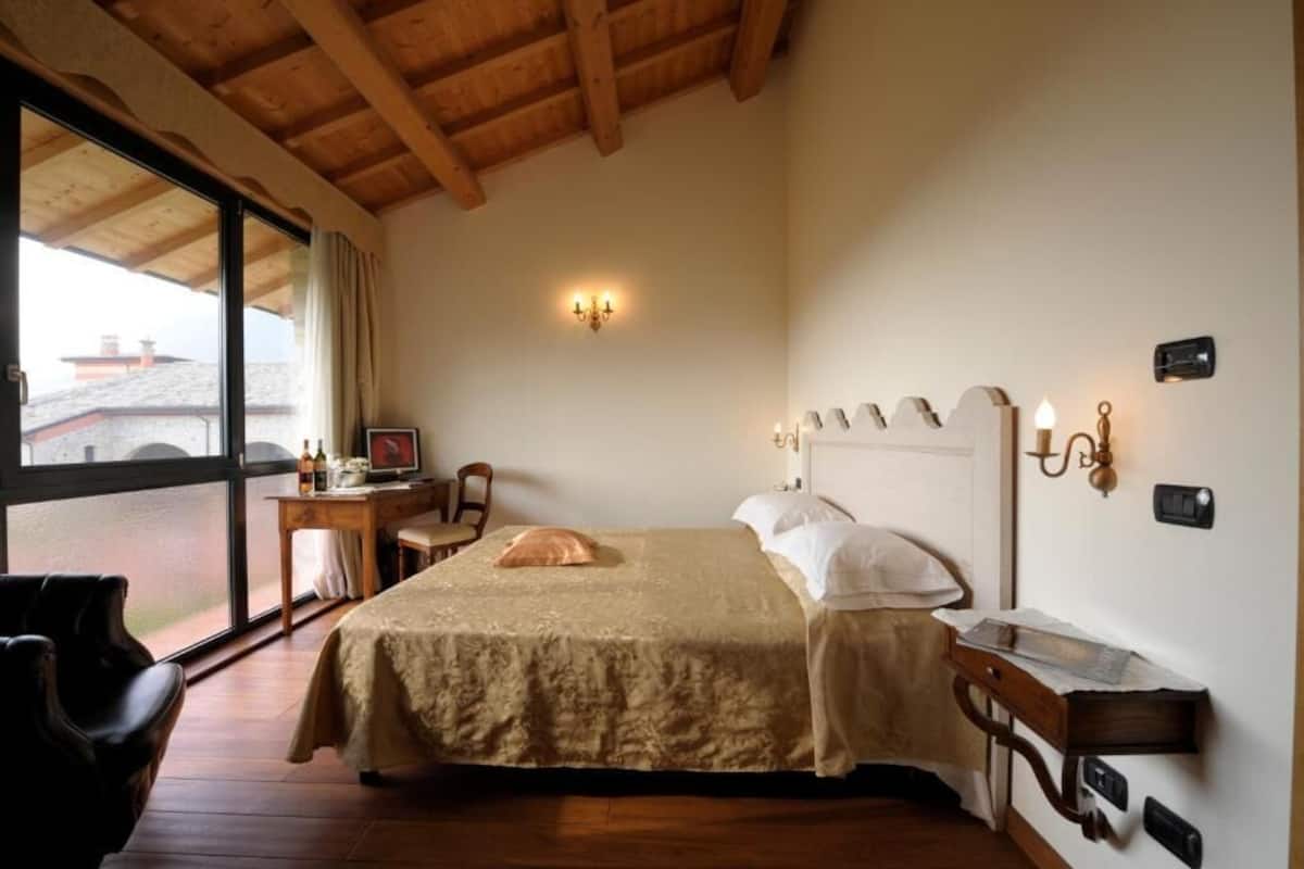 Een slaapkamer met een groot bed, een bureau en een stoel. Er is een raam met uitzicht op gebouwen.