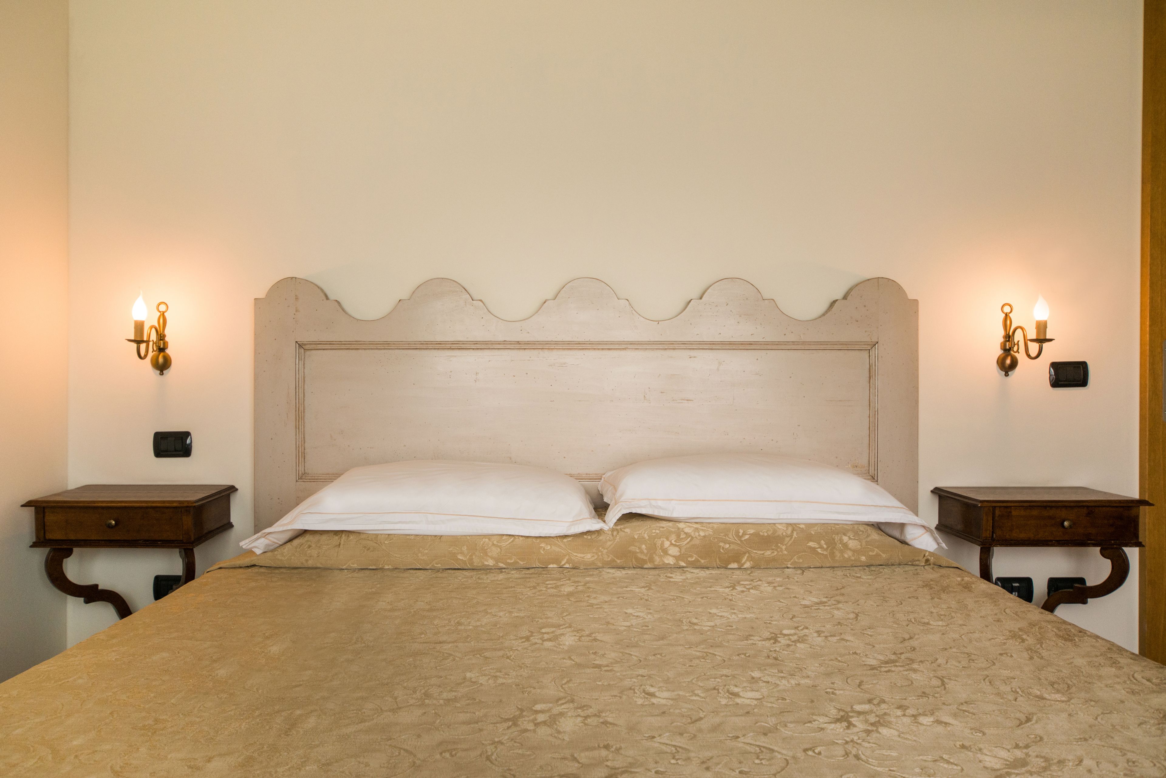 Un lit avec une tête de lit, deux tables de chevet et des lampes fixées au mur.