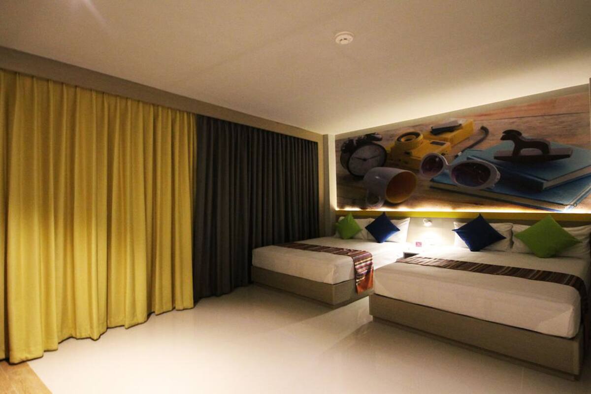 Una habitación de hotel con dos camas, un cuadro grande sobre ellas y una cortina en un lateral.