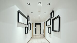 A hallway with a light wooden floor and white walls, featuring multiple black-framed pictures on the walls. - Three Sukhumvit Hotel (Bangkok)