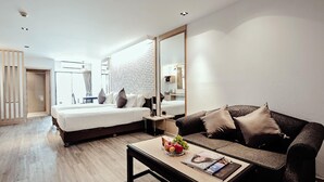 A modern hotel room with a bed, a sofa, a coffee table with fruit and a magazine, and a large mirror. - Three Sukhumvit Hotel (Bangkok)