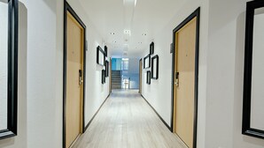 A corridor with wooden doors, framed pictures on the walls, and a staircase in the distance. - Three Sukhumvit Hotel (Bangkok)