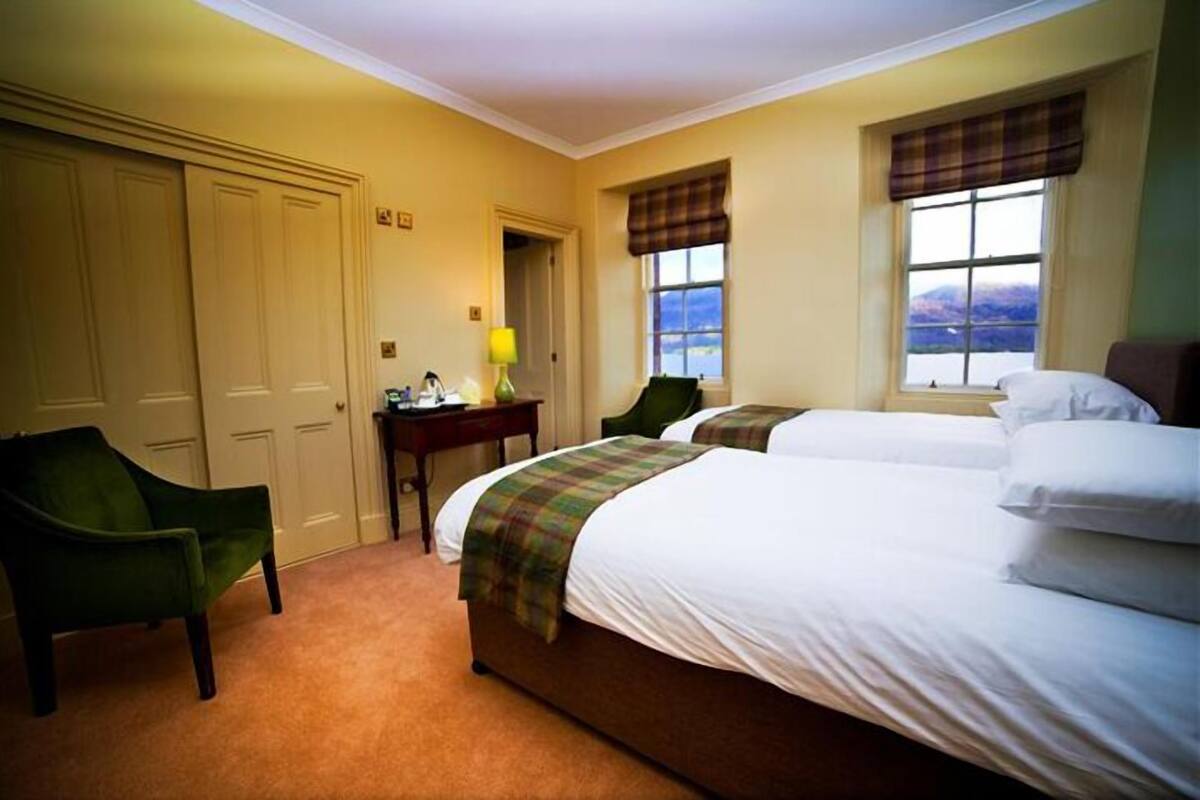 Une chambre d’hôtel avec deux lits, un bureau avec une lampe, une chaise et une vue sur l’extérieur.