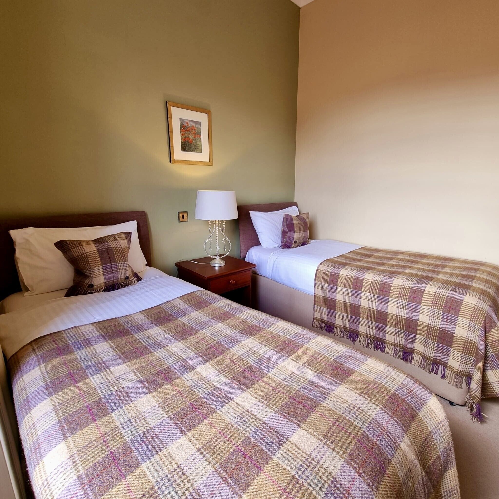 A hotel room with two beds, a nightstand with a lamp, and a framed picture on the wall.