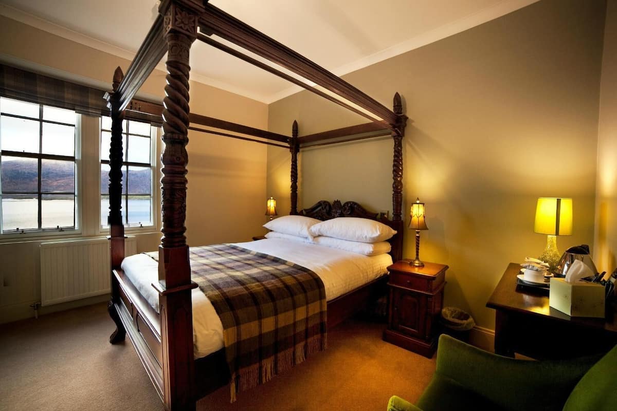 Un lit à baldaquin avec une couvre-lit à carreaux, des lampes de chevet, une table de chevet et une vue sur l’extérieur grâce à de grandes fenêtres.