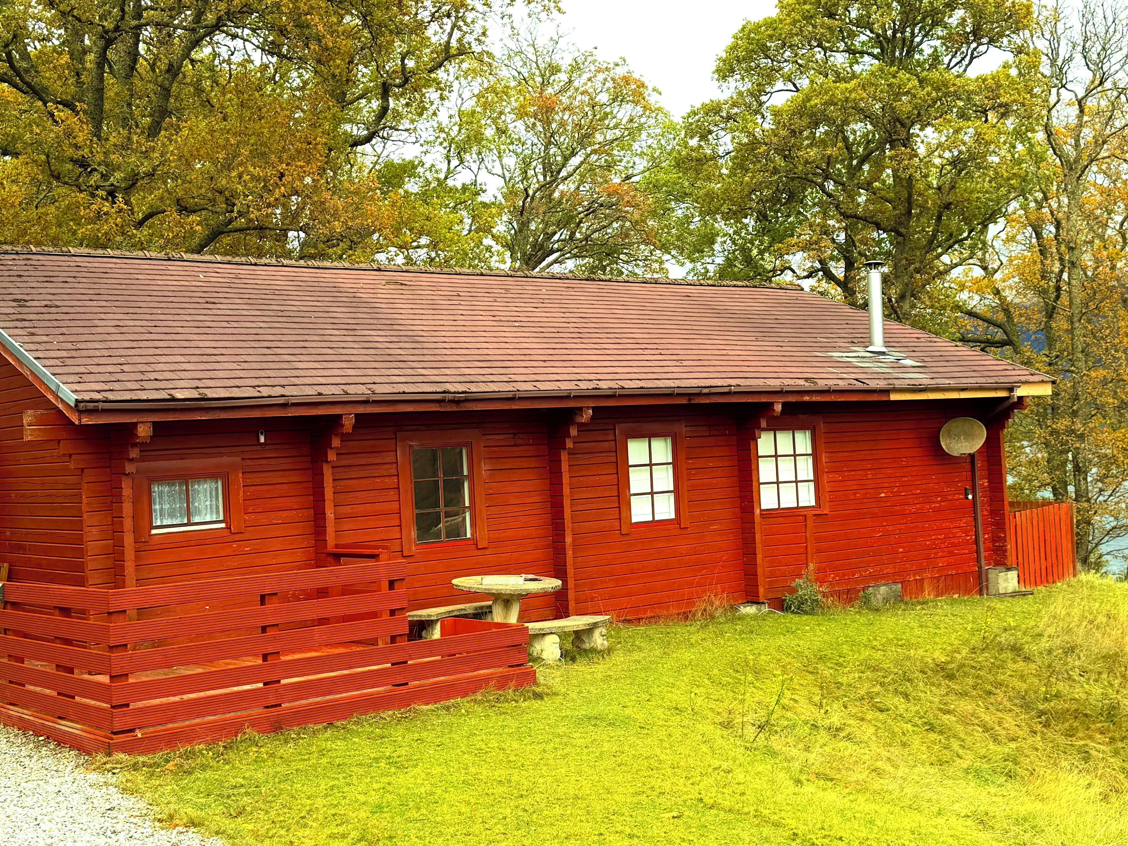 A red wooden cabin with a sloped roof, a front porch, and a small stone table.