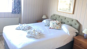 Una cama bien hecha con un cojín floral y un cabecero tapizado en una habitación con papel pintado a rayas y un cuadro en la pared.