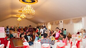 Un salón de banquetes con mesas redondas, sillas blancas con cintas rojas y una gran lámpara de araña.