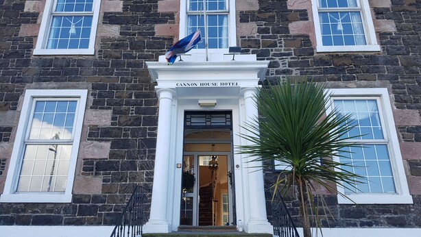 Un edificio histórico con fachada de piedra, detalles blancos y una entrada central con toldo.