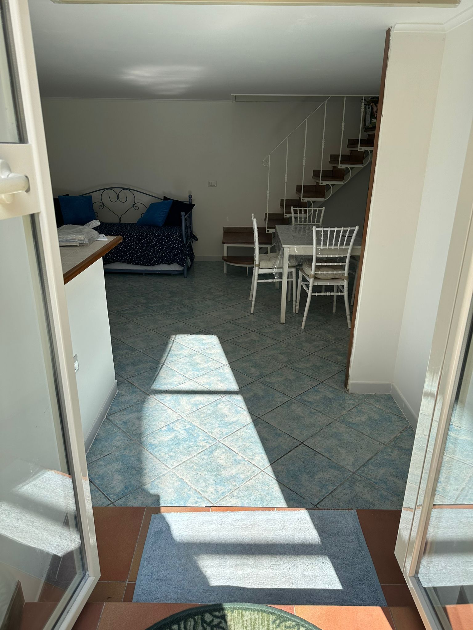 A room with a bed, a dining table with chairs, and a staircase.