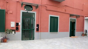 Um edifício com uma porta verde, uma janela com persianas verdes e uma planta em vaso na parte externa.