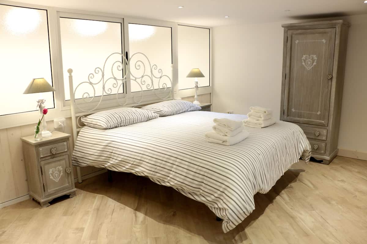 Una cama bien hecha con ropa de cama a rayas, una mesita de noche con lámpara y un armario.
