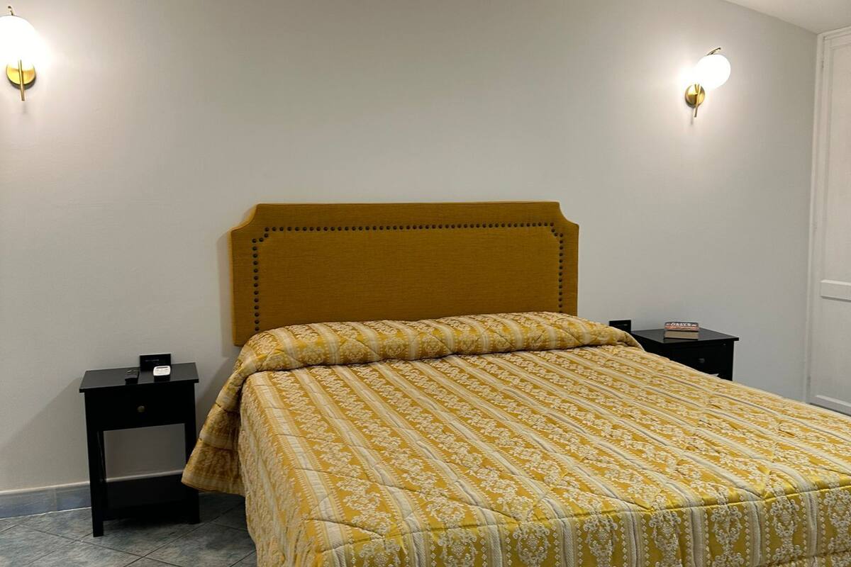 Un dormitorio con cama, dos mesitas de noche y dos luces fijadas a la pared.