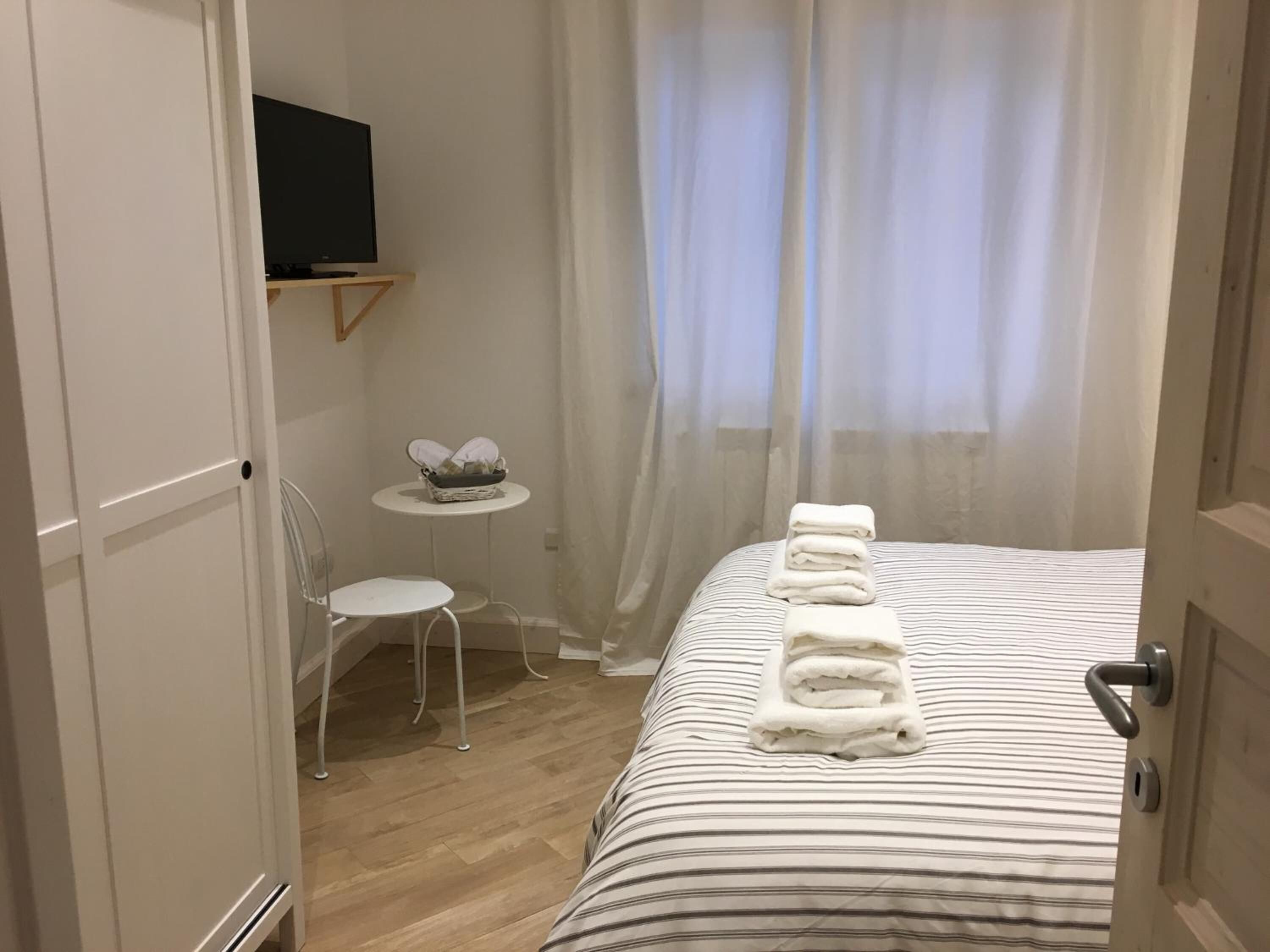 Een hotelkamer met een bed, een kleintje tafeltje met een mand, een stoel en een aan de muur bevestigde televisie.